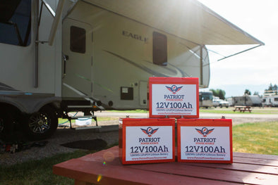Patriot Power Source batteries on a picnic table infront of an RV