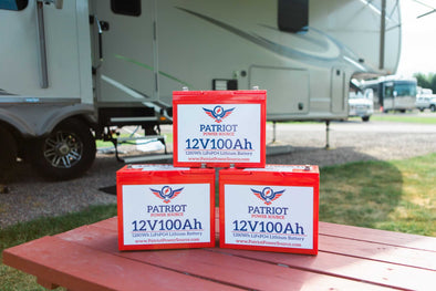 Stack of Patriot Power Source batteries on a table infront of an RV